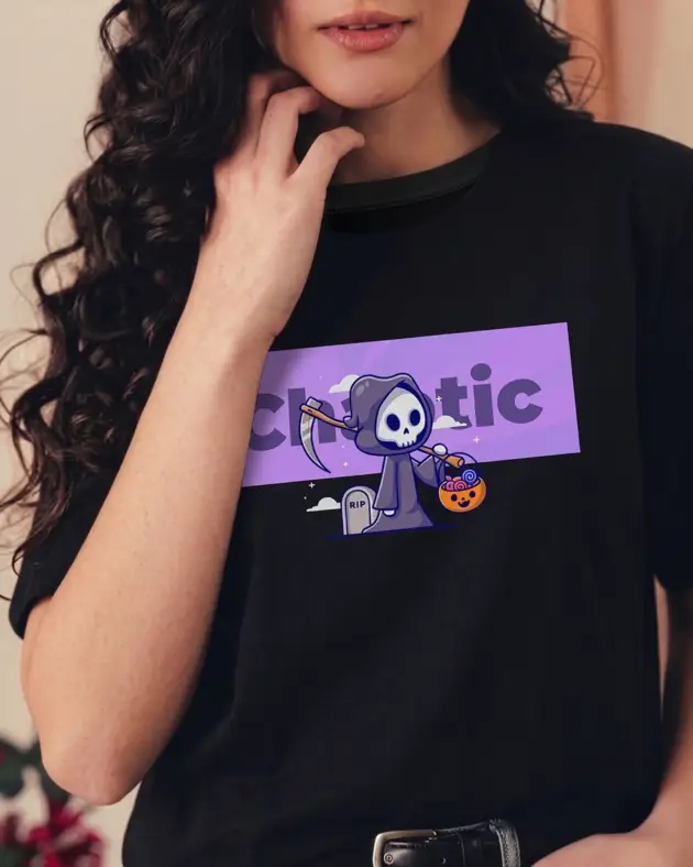 Young woman wearing a black t-shirt with a purple "Chaotic" graphic featuring a cute cartoon Grim Reaper holding a pumpkin candy bucket.