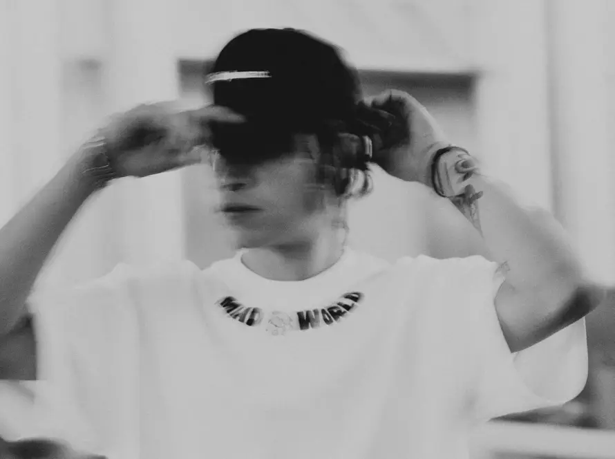 A person wearing a white oversized "MAD WORLD" streetwear t-shirt and a black baseball cap, showcasing urban fashion in Pakistan.