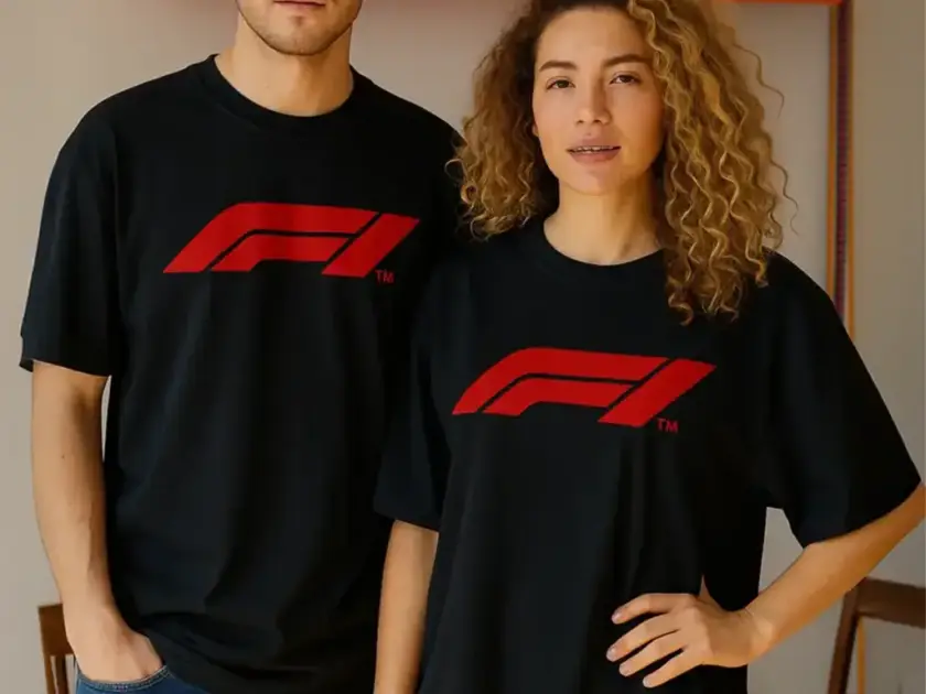 A man and a woman wearing matching Mint Macro black oversized t-shirts with a bold red F1 racing logo on the chest.