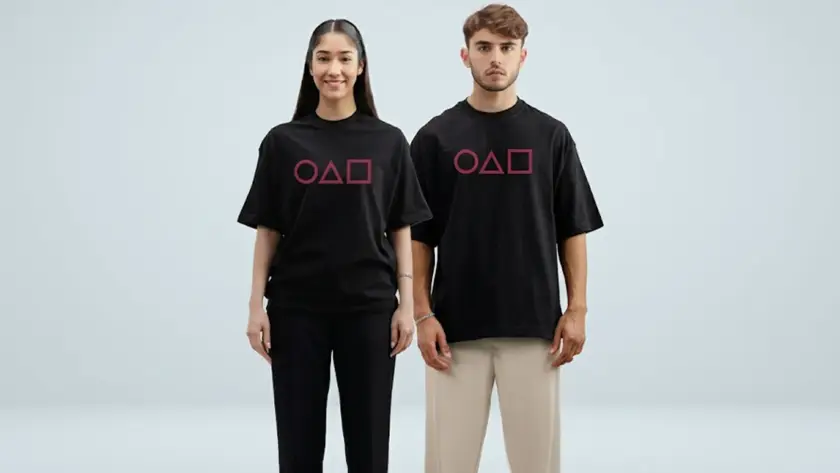 A male and female model wearing matching black oversized t-shirts with pink Squid Game inspired circle, triangle, and square symbols.