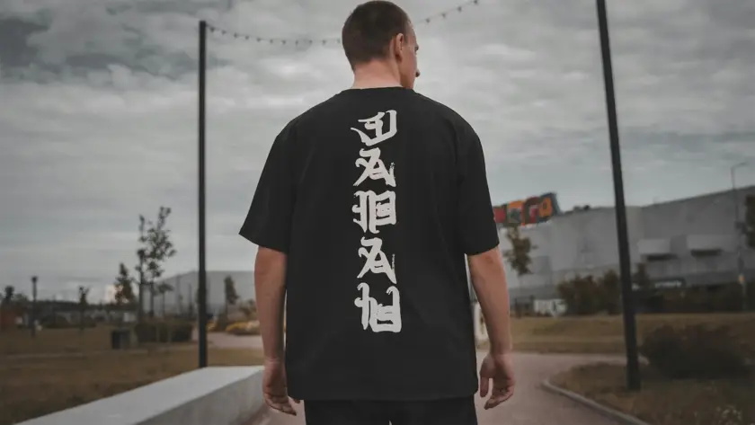 Back view of a man wearing a Mint Macro black oversized t-shirt featuring vertical white Japanese calligraphy-style typography.