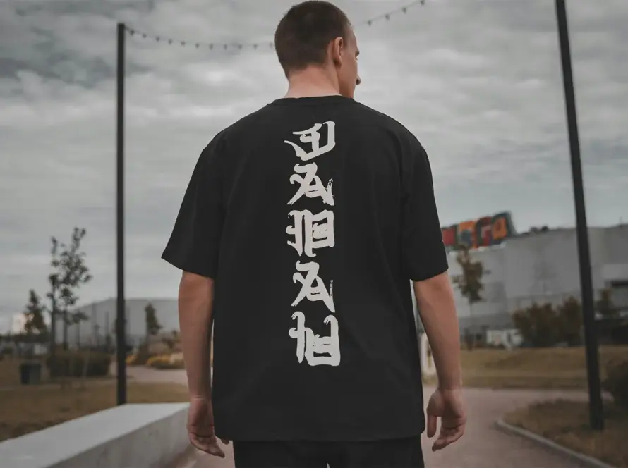 Back view of a man wearing a Mint Macro black oversized t-shirt featuring vertical white Japanese calligraphy-style typography.