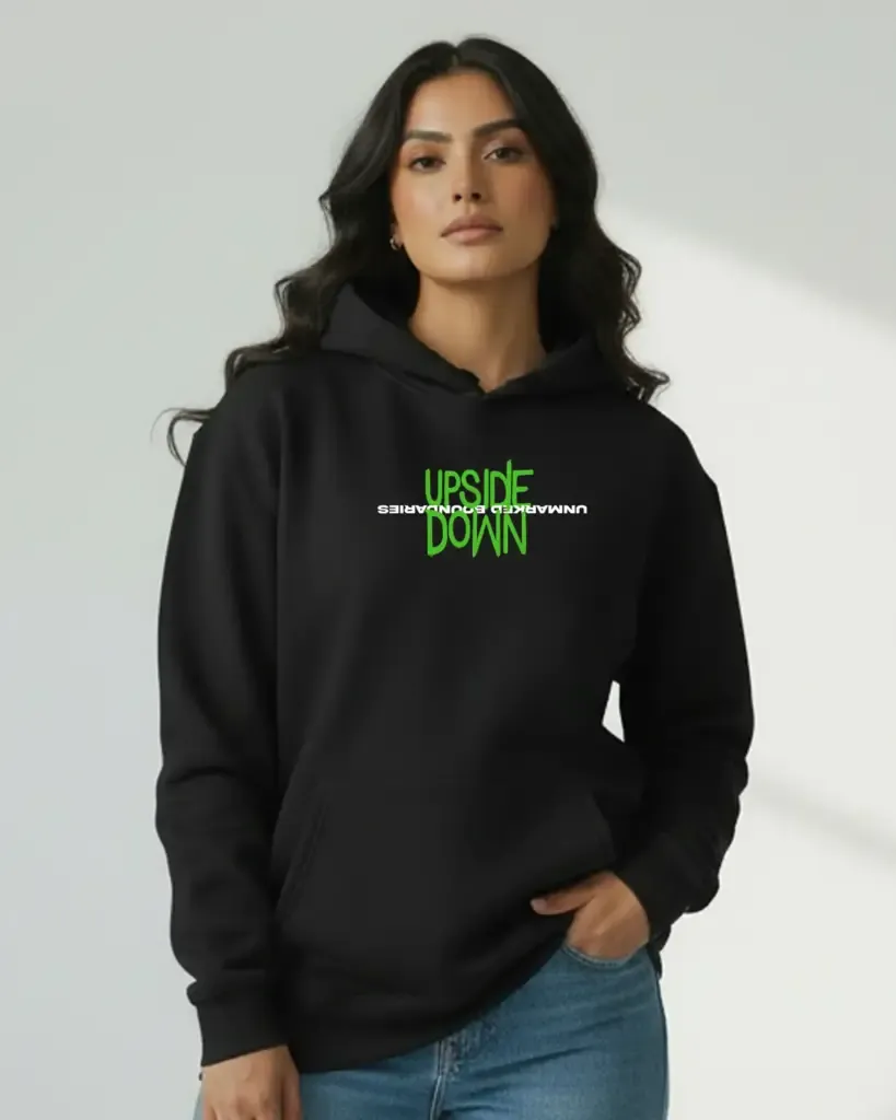 A woman modeling a black hoodie with a neon green graphic that reads "UPSIDE DOWN" mirrored across a white text line saying "UNMARKED BOUNDARIES."