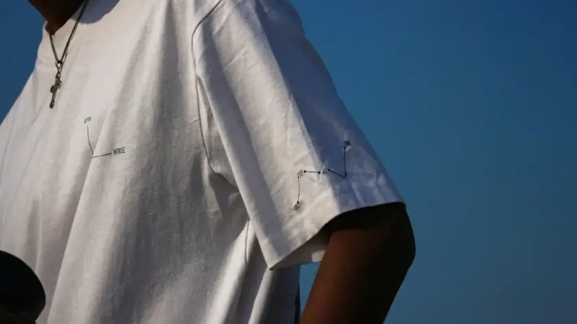 Close-up of a white oversized t-shirt featuring minimalist black graphic line art on the chest and sleeve against a clear blue sky.