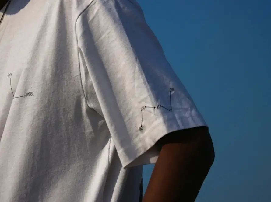 Close-up of a white oversized t-shirt featuring minimalist black graphic line art on the chest and sleeve against a clear blue sky.