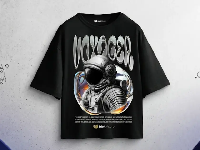 A black oversized streetwear t-shirt by Mint Macro featuring a large graphic of an astronaut in a chrome bubble with "VOYAGER" in wavy retro-futuristic typography.