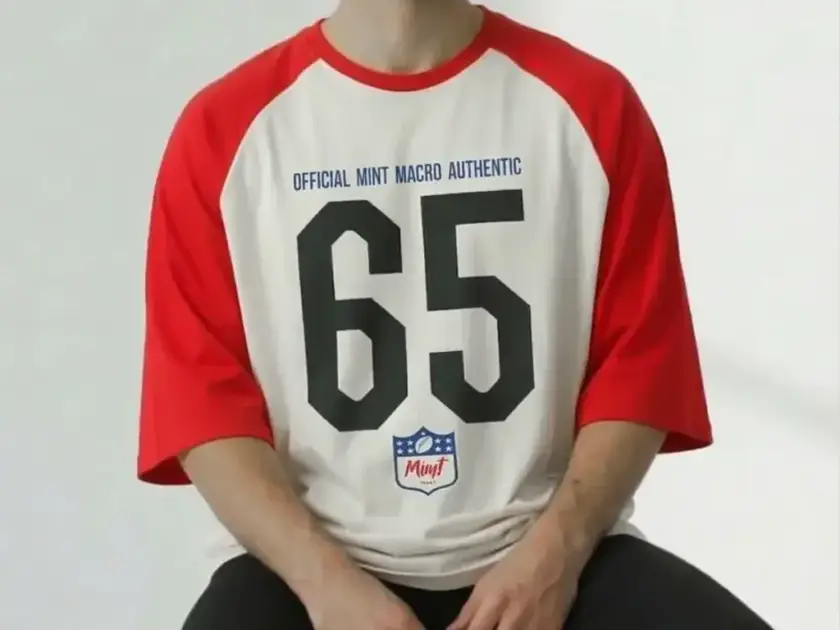 A close-up of a person wearing a Mint Macro "Official Authentic 65" raglan t-shirt with red sleeves and a white body.