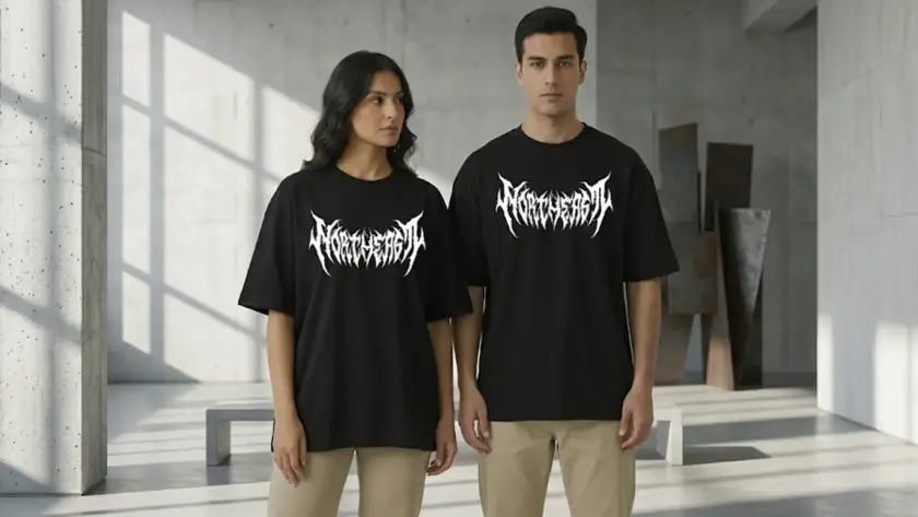 A man and woman standing together wearing matching black oversized t-shirts with a white heavy-metal style graphic on the chest in a modern industrial setting.