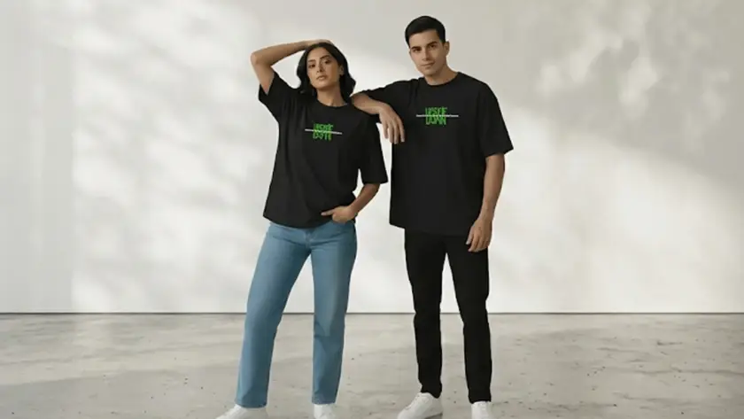 A man and a woman posing together in matching oversized black t-shirts with a green "Upside Down" graphic in a minimalist studio.