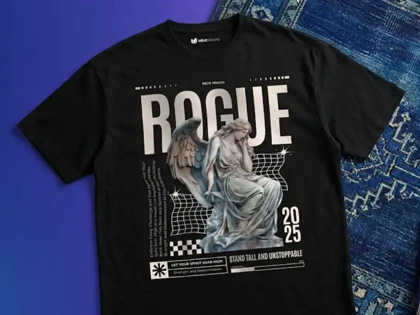 A black oversized t-shirt featuring a large "ROGUE" graphic with a classical angel statue, Y2K aesthetic grid patterns, and the year 2025, laid flat next to a blue patterned rug