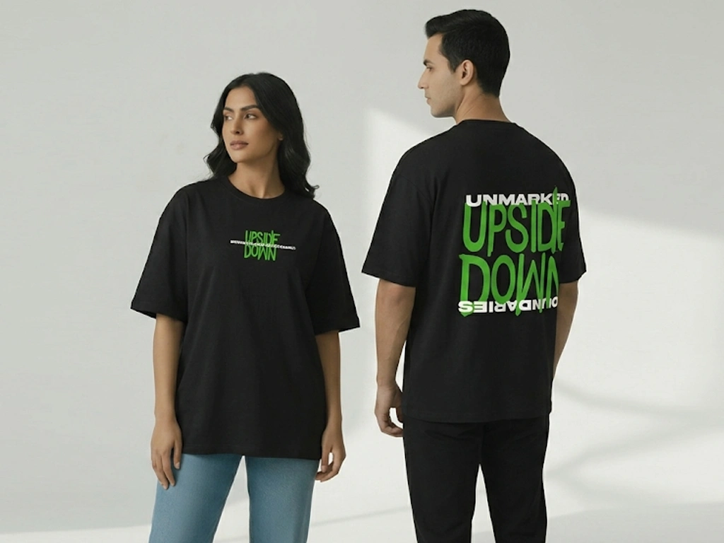 Man and woman modeling Mint Macro's "Upside Down" oversized black streetwear t-shirt, showing the minimalist front graphic and the bold green and white typography back print.