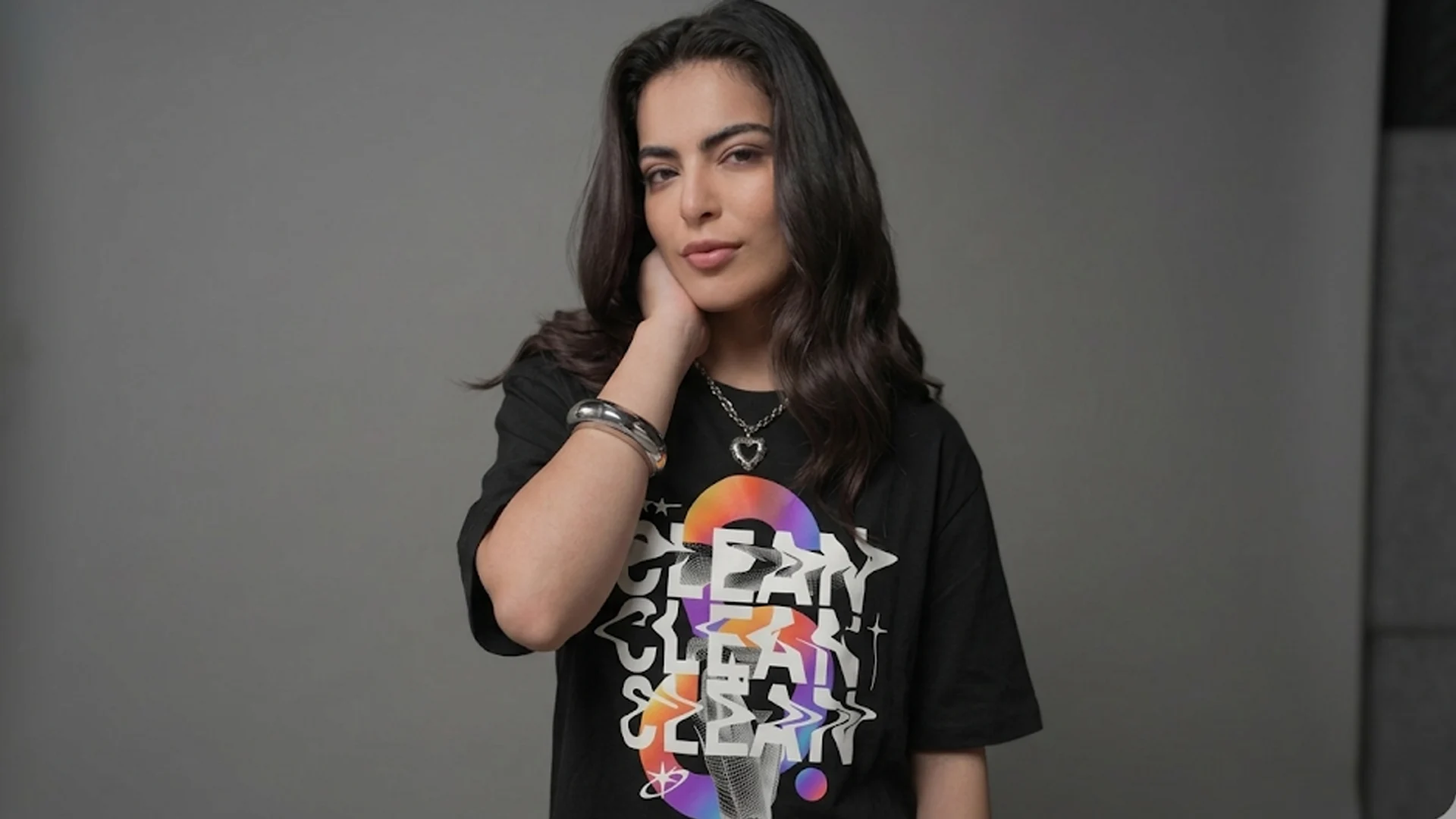 A woman modeling the Mint Macro "Clean" black oversized t-shirt against a grey studio backdrop, highlighting the wavy, multi-colored retro-futuristic graphic print on the front.