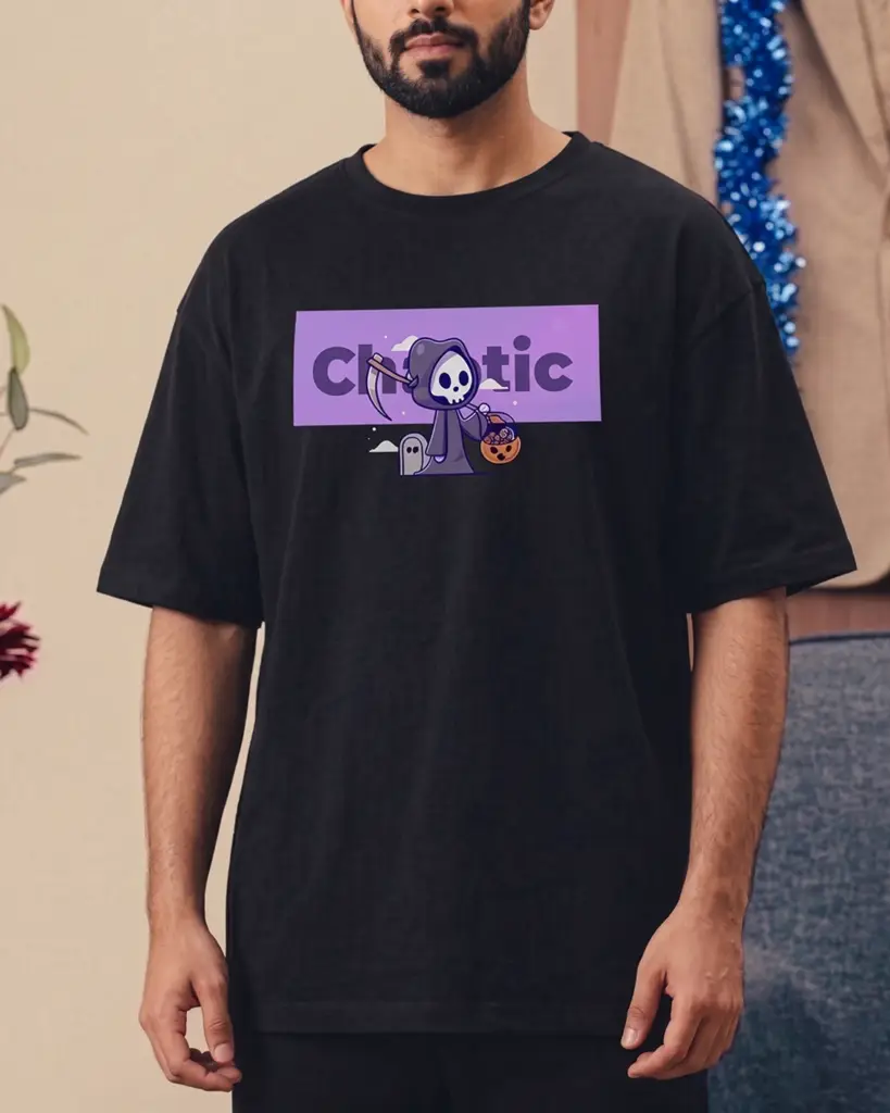 A man wearing an oversized black t-shirt featuring a purple rectangular graphic that reads "Chaotic" behind a cute cartoon grim reaper holding a scythe and a pumpkin basket.