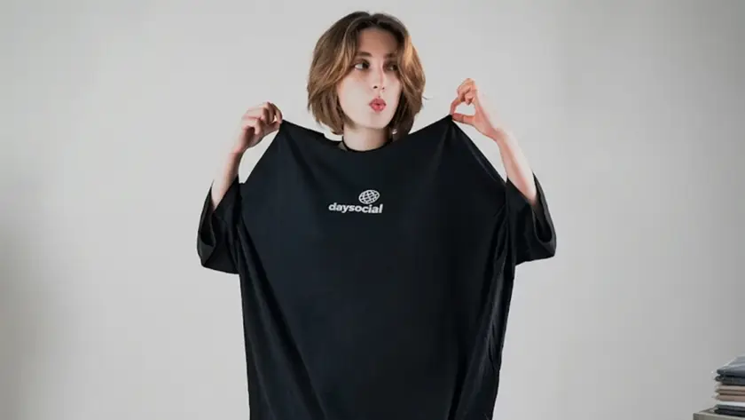 An oversized black crewneck t-shirt featuring a small white graphic on the center chest with the word "daysocial" written below a stylized grid globe icon.