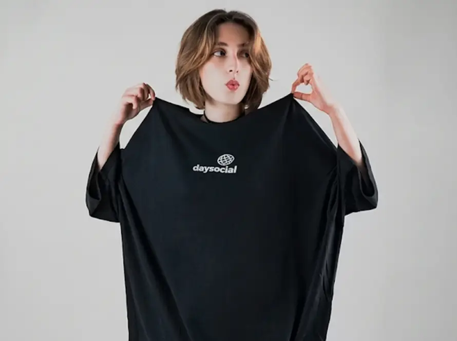 An oversized black crewneck t-shirt featuring a small white graphic on the center chest with the word "daysocial" written below a stylized grid globe icon.